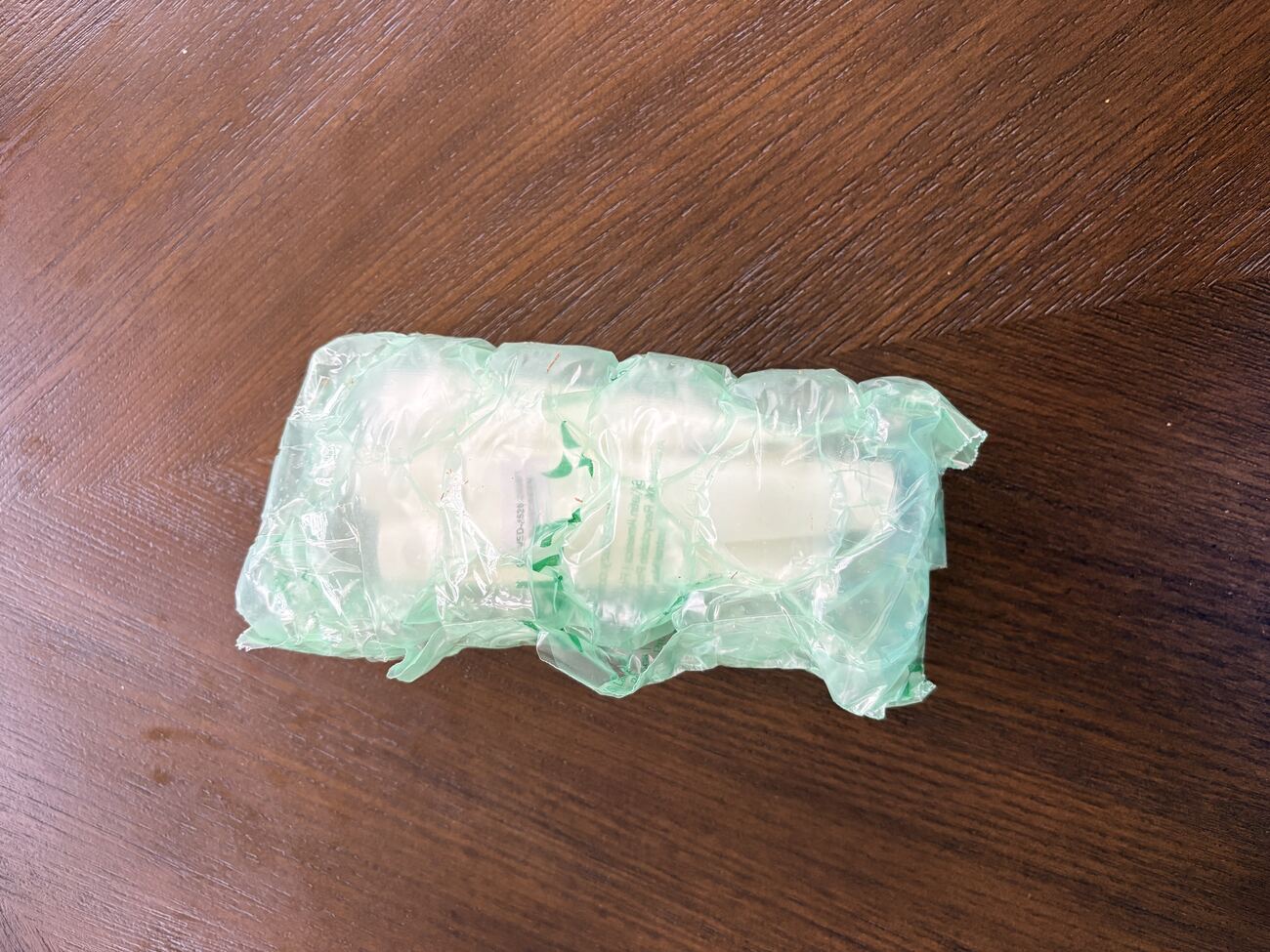 A small package wrapped in green bubble wrap, photographed from above on a dark wooden surface.